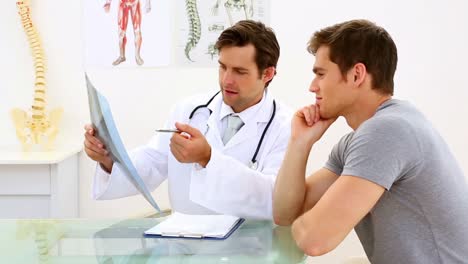 un médico serio discutiendo radiografías con su paciente.
