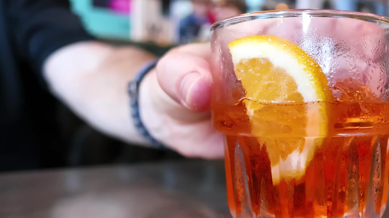 A person holds a refreshing orange drink with a slice, seated in a comfortable booth.