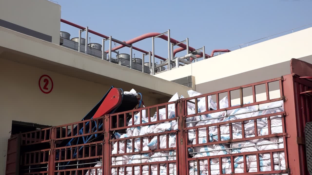 Processing chemical fertilizer, sugar, flour, and rice sacks stacked up bags on a conveyor belt in large warehouse to truck for distribution to customer, import export logistics business