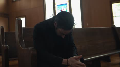 jovem de fato preto sentado em um banco na igreja orando em adoração em câmera lenta cinematográfica