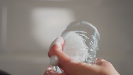 close up of hand holding soapy glass tumbler carefully observing for cleanliness showing bubbles soap foam around cup surface focus on hygiene neatness and attention under soft light in kitchen