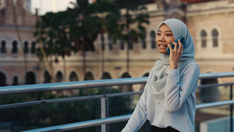 young woman in hijab talking on mobile phone outdoors in city
