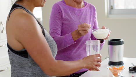 dos mujeres mayores felices y diversas preparando cócteles y sonriendo en la cocina, en cámara lenta