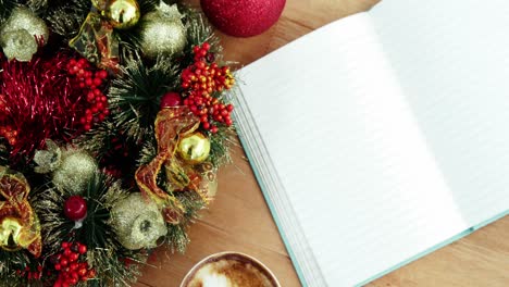 Close-up-of-coffee-cup-with-christmas-decoration-and-notebook