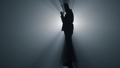 silhouette believer praying in dark space. serious man standing folded hands.