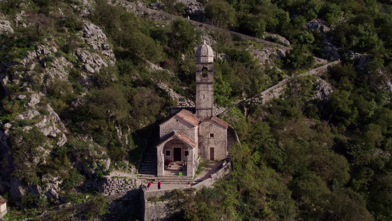 Toma aérea de ciudad medieval, iglesia, bosque, montaña y sendero en la Bahía de Kotor