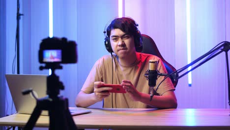 asian man playing video game with mobile phone then pose and smiles to camera while live stream