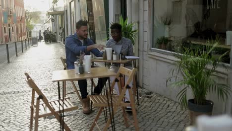 young men using laptop and discussing work in outdoor cafe