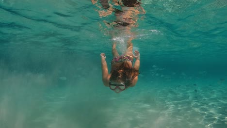 Underwater-scene-of-red-hair-little-girl-swimming-in-incredible-crystal-clear-tropical-sea-water-of-exotic-island