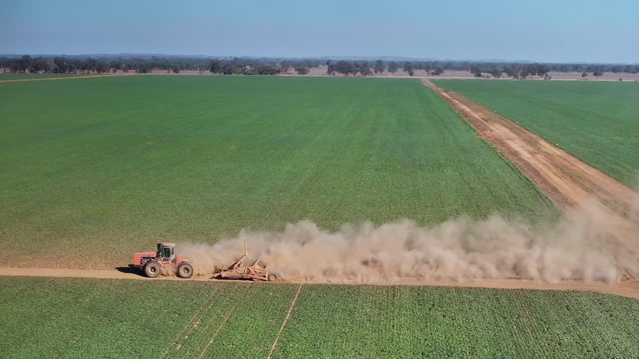 Trator e pequena motoniveladora dirigindo por uma estrada de terra com plantações e fazendas ao fundo