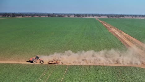 tractor and small grader driving down a dirt road with crop and farms beyond