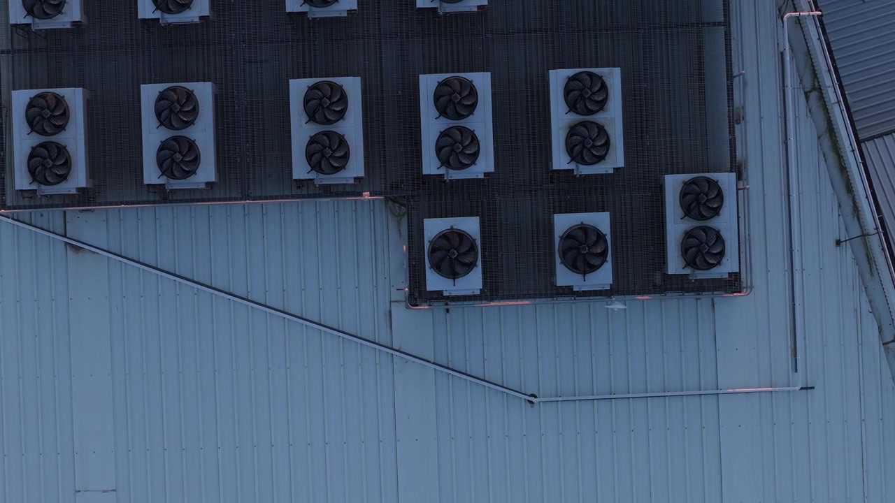 Multiple air conditioning units with spinning fans on an industrial building's corrugated metal roof