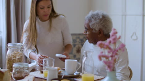 black elderly man having breakfast when woman bringing him pills