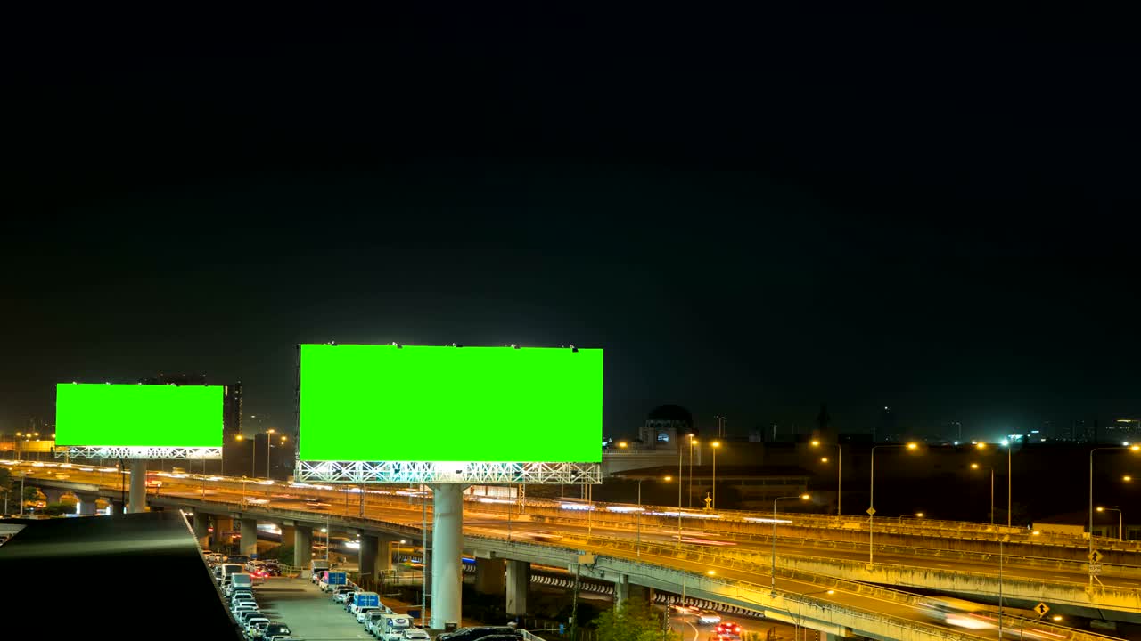 Grøn skærm på reklameskilt på motorvej om natten med bybaggrund i Bangkok, Thailand. Time-lapse.