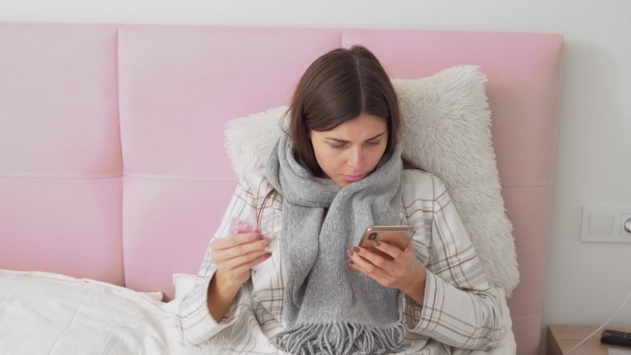 ragazza malata sdraiata a letto leggendo al telefono di pillole e bevendo tè