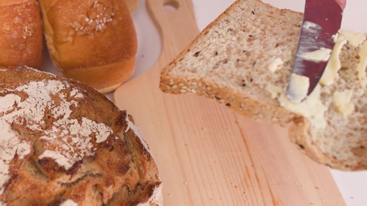 Close-up shot of a knife spreading peanut butter on multigrain bread over a wooden board.