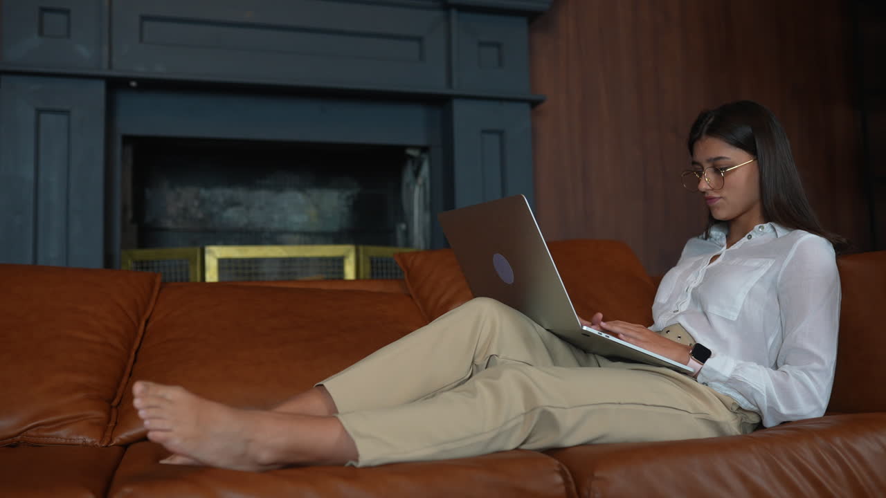 여성이 소파에서 휴식을 취하고 노트북에서 일하고 있습니다.