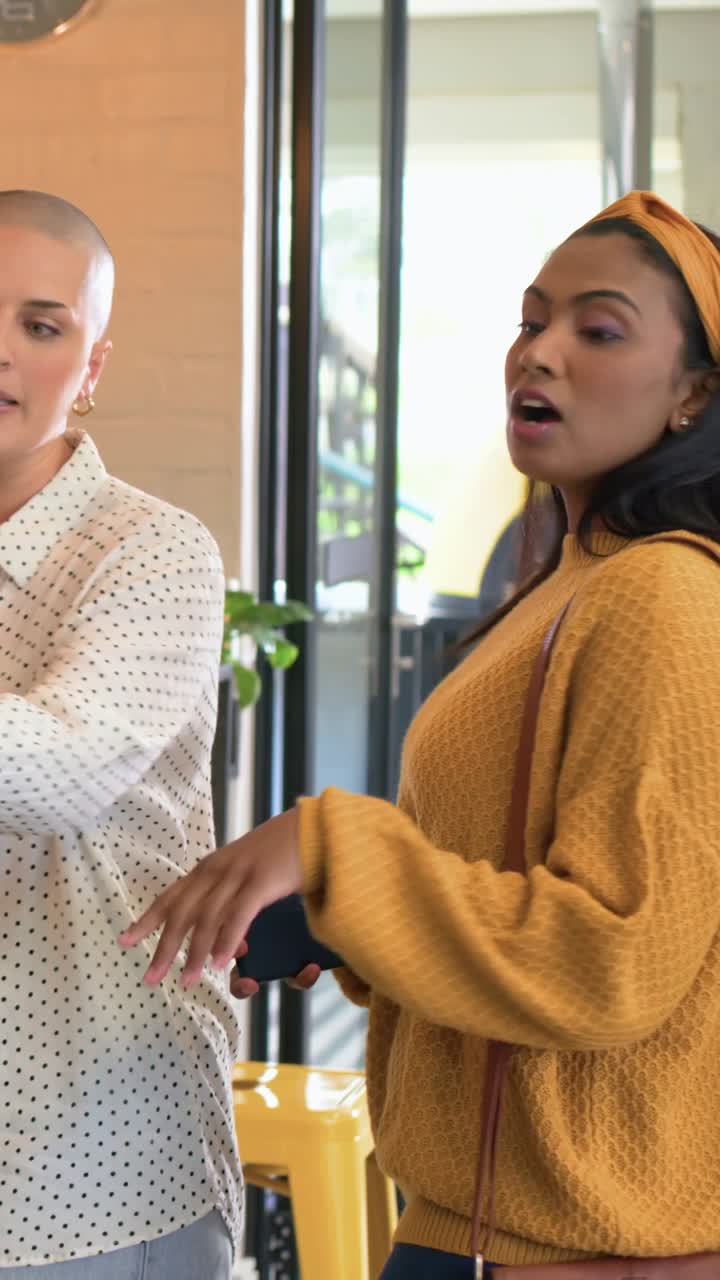 Vertical video: Talking woman in polka-dot top pointing at cafe counter, mustard top holding phone