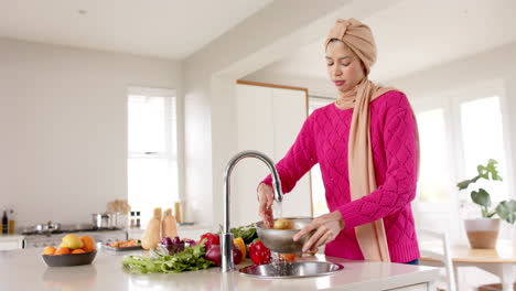 biracial woman in hijab washing food in kitchen at home with copy space, slow motion