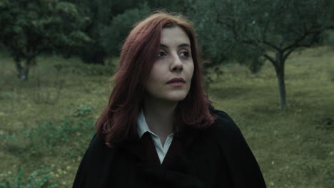 young woman with red hair looks around in a public park in cloudy cold day