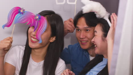 group of young friends having fun posing in photo booth with props shot in slow motion