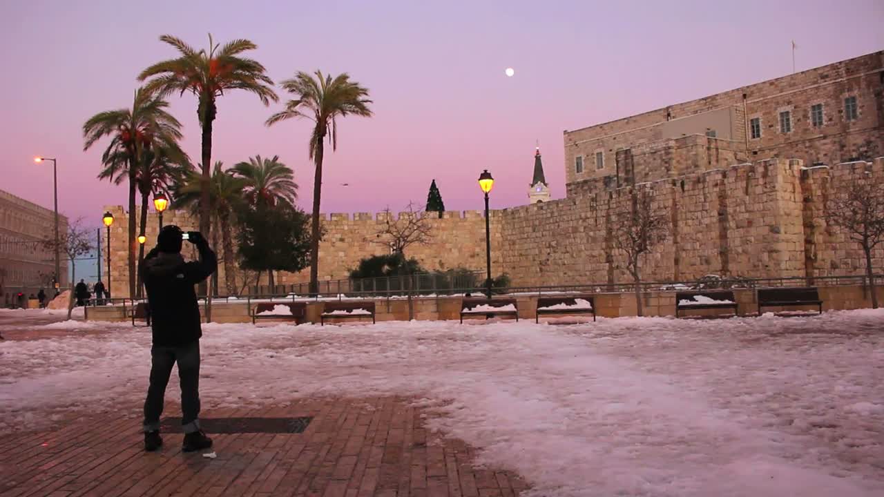 한 남자가 드문 눈이 내린 뒤 황혼에 예루살렘의 광장에 서 있다