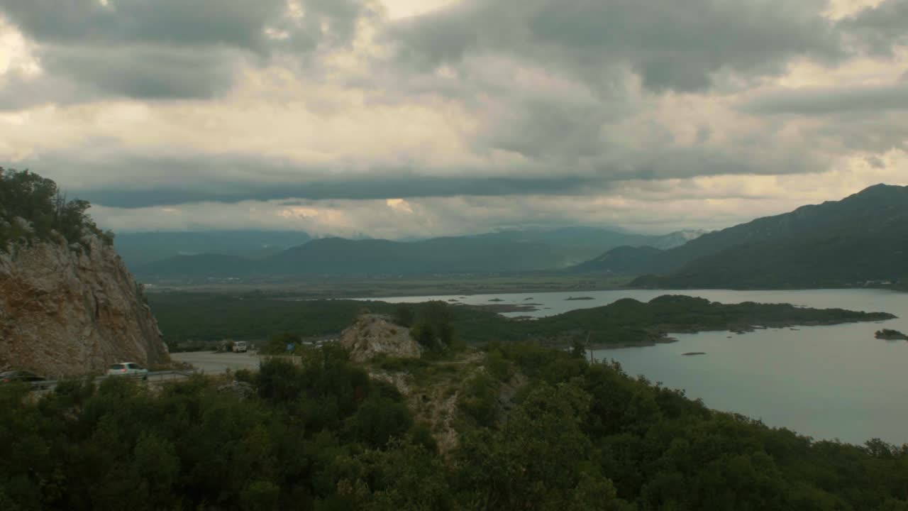 dos coches pasan por una carretera de montaña con curvas junto a un hermoso lago