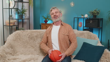 mature man sitting on sofa with basketball tossing and spinning ball enjoying playing at home