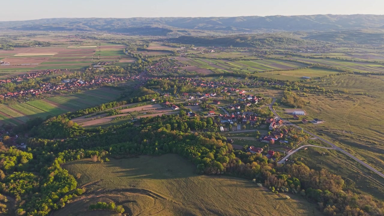 Luchtfoto van een landelijk landschap met akkerland, glooiende heuvels en een klein dorp omgeven door groen.