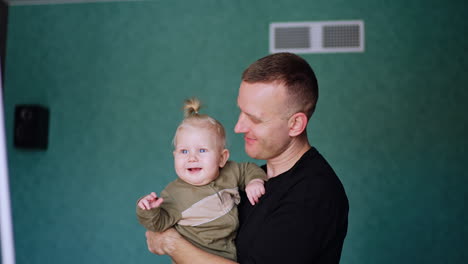 man holds a cute little blond baby. lovely child looks ahead attentively smiling adorably.
