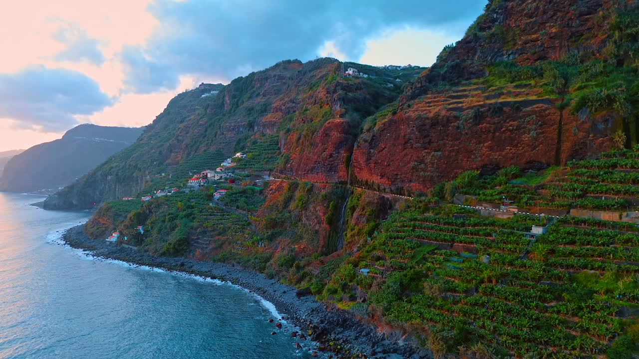 Steep mountains with banana gardens and some cottages on the slopes. Picturesque coast of Madeira, Portugal.