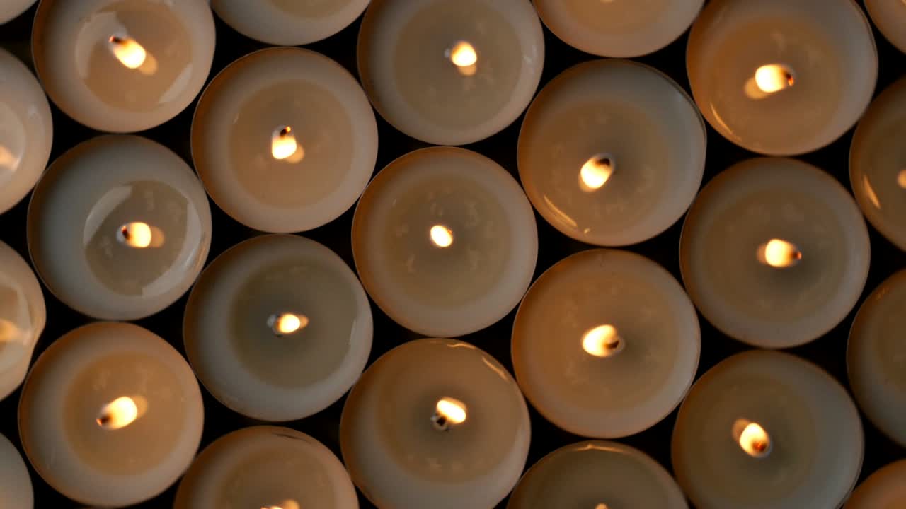 Molte piccole candele rotonde con riflessi ardenti stanno bruciando nell'oscurità.