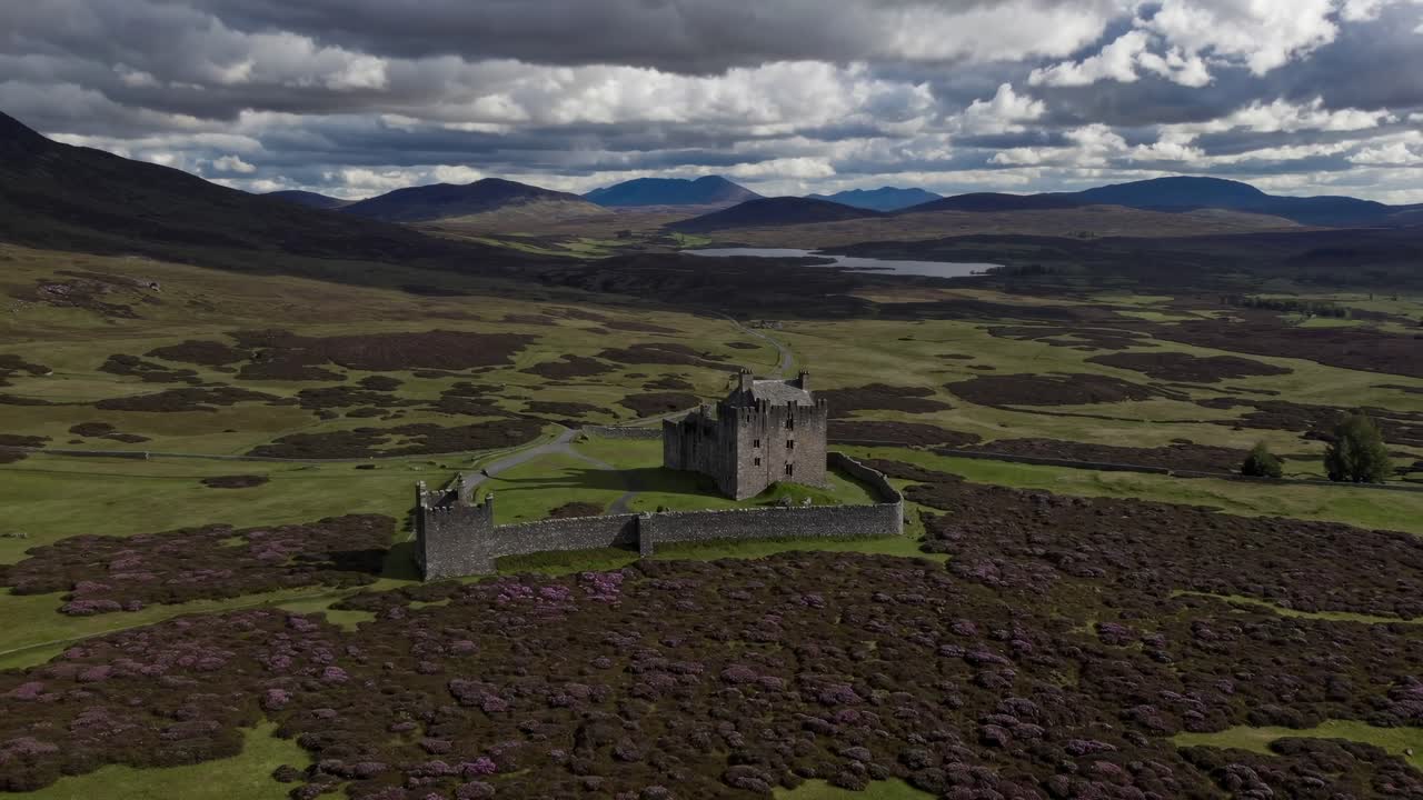Aerial video of a medieval castle surrounded by lush green fields and mountains