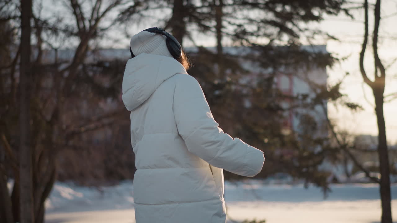 Free spirit swirling in snowy landscape wearing white puffer jacket and beanie with headphones under golden sunset light captured in motion against blurred forest backdrop evoking joyful freedom