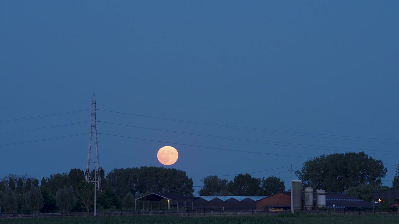 Bulan Stroberi di balik peternakan pedesaan yang indah saat senja dengan bulan purnama yang terbit di langit biru cerah. Pemandangan pedesaan yang tenang, pencahayaan atmosferik, warna-warna cerah, gerakan halus.