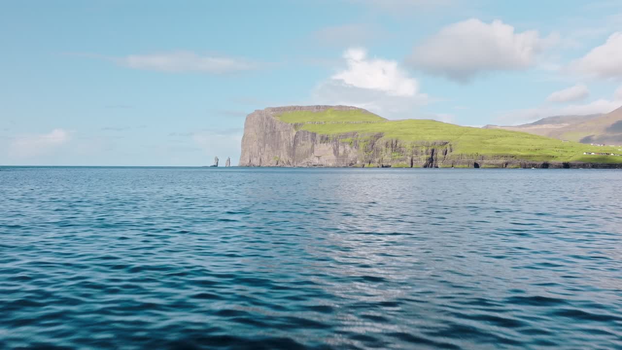 A serene coastal view of cliffs and grassy hills in the Faroe Islands, under sunny skies