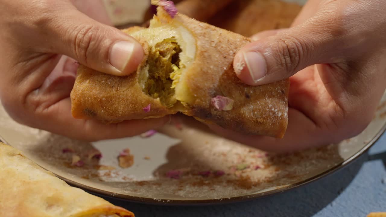 Close-up shot of hands breaking a traditional Moroccan briwat pastry, revealing a golden, crispy texture and delicious meat filling. Authentic Moroccan street food, perfect for Ramadan