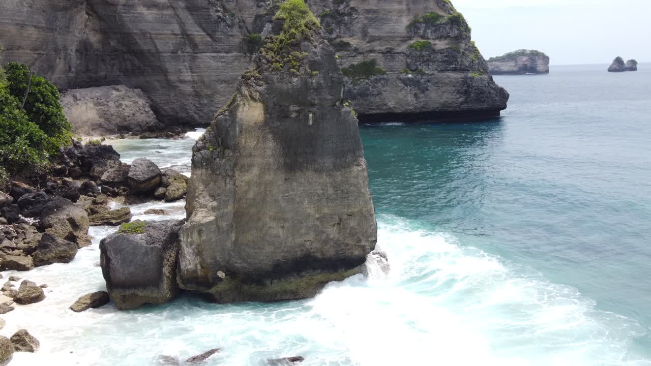 Aerial, Waves pounding a Diamond-shaped basalt rock topped with Rock cap Moss at Diamond Beach on Nusa Penida Island