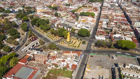 Aerial-drone-view-of-an-iconic-city-roundabout-with-a-striking-yellow-monument,-surrounded-by-historic-buildings-and-bustling-traffic