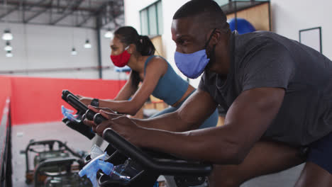 diverse woman and man wearing face masks exercising at gym