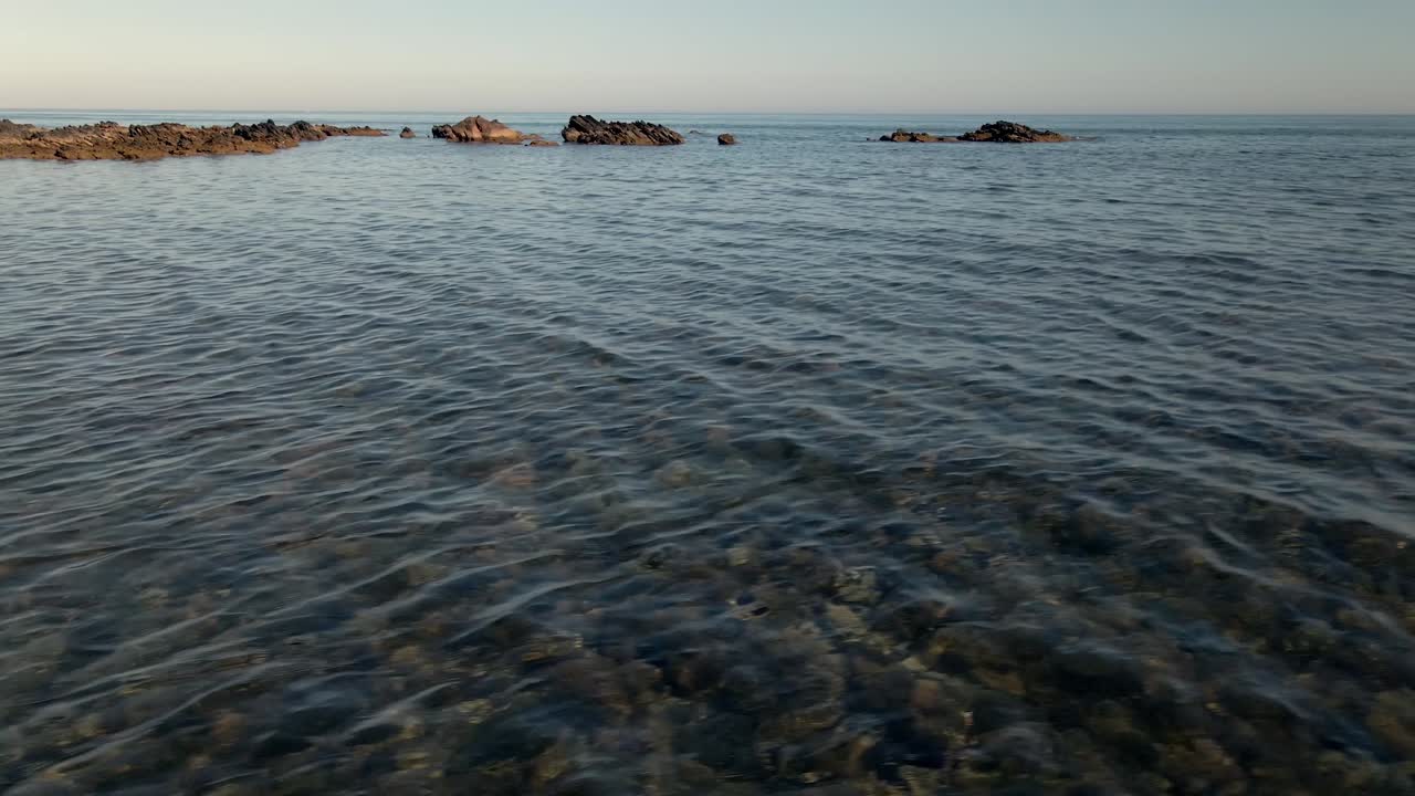 Vista dal basso sopra un oceano limpido e trasparente, panoramica verso l'alto su una formazione rocciosa, l'orizzonte marino e la costa.