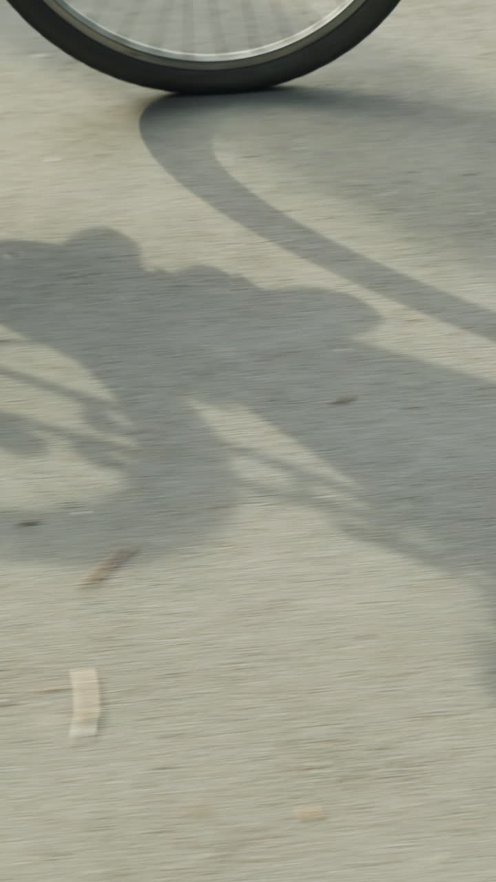 스니커와 검은색 바지를 입은 자전거 타는 자전거 운전자가 이 비는 날에 천천히 자전거를 타고 자전거의 하고 은 그림자를 만들어 빛으로 빛나는 도로에 던집니다.