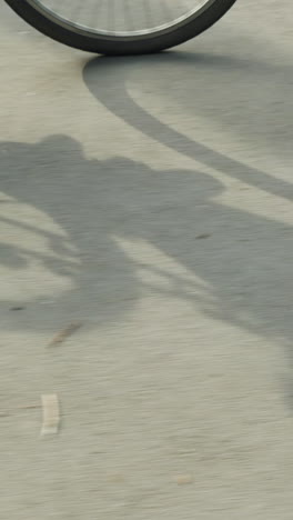 ciclista con zapatillas deportivas y pantalones negros pedaleando la bicicleta lentamente en un día soleado, creando una sombra distinta y clara de la bicicleta arrojada a la carretera iluminada por el sol