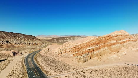 a desert highway with sandstone cliffs and buttes on both sides - sliding aerial view