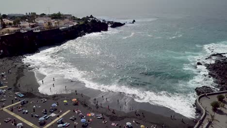 Drone-Vuela-Sobre-La-Playa-De-La-Arena-Llena-De-Turistas-Durante-Las-Vacaciones,-Imágenes-Aéreas-De-La-Isla-De-Tenerife