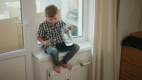 child pouring water from a jug into a glass at a window