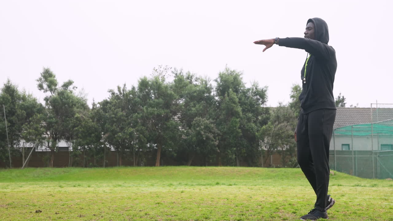 Playing soccer, athlete jumping and pointing on grassy field with trees behind
