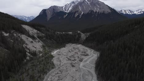 Luftaufnahme-Eines-Ausgetrockneten-Baches,-Umgeben-Von-Alpinem-Grünem-Wald-Mit-Felsigem-Berghintergrund-Mit-Schnee-Oben,-Tilt-Up-Aufnahme,-Naturschutzkonzept