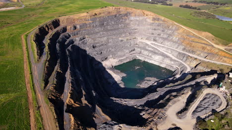 drone tilt-up view of open-cast surface mine in lush hilly landscape, quarrying