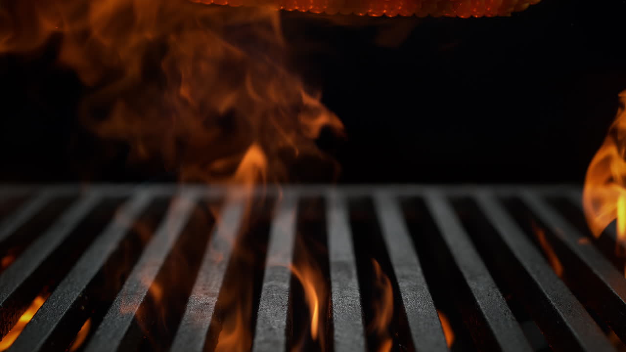 Corn Cob Falling Onto the Charcoal Grill on the Black Background, Flames Burst From Beneath The Grill Grate in Slow Motion